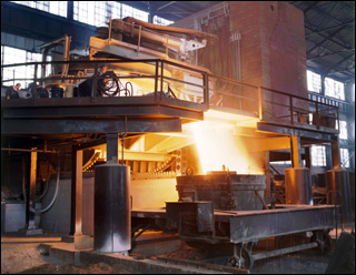 Photo inside the Brackenridge stell mill of a tilted 35-ton electric furnace pouring white-hot steel into a trough below, flying sparks indicate the fluidity of the steel.