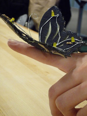 Photo of a fabric butterfly with several LEDs on its wings, perched on a person’s hand.