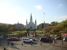 A church sits in the background as cars and people walk by.