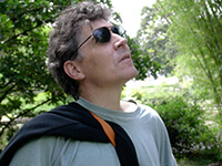 A headshot of a white man standing in front of trees looking up.