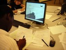 A student sits in front of a computer doing calculations. On the screen is an image of a large sphere on top of a building.