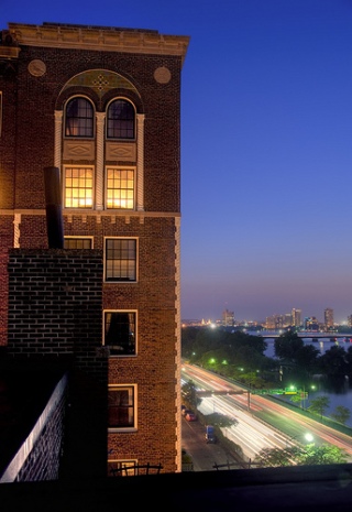 Photograph of a brick building against a deep blue sky, with the city visible in the background.