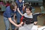 A girl is holding a boot with wires on it. An adult volunteer is helping her.